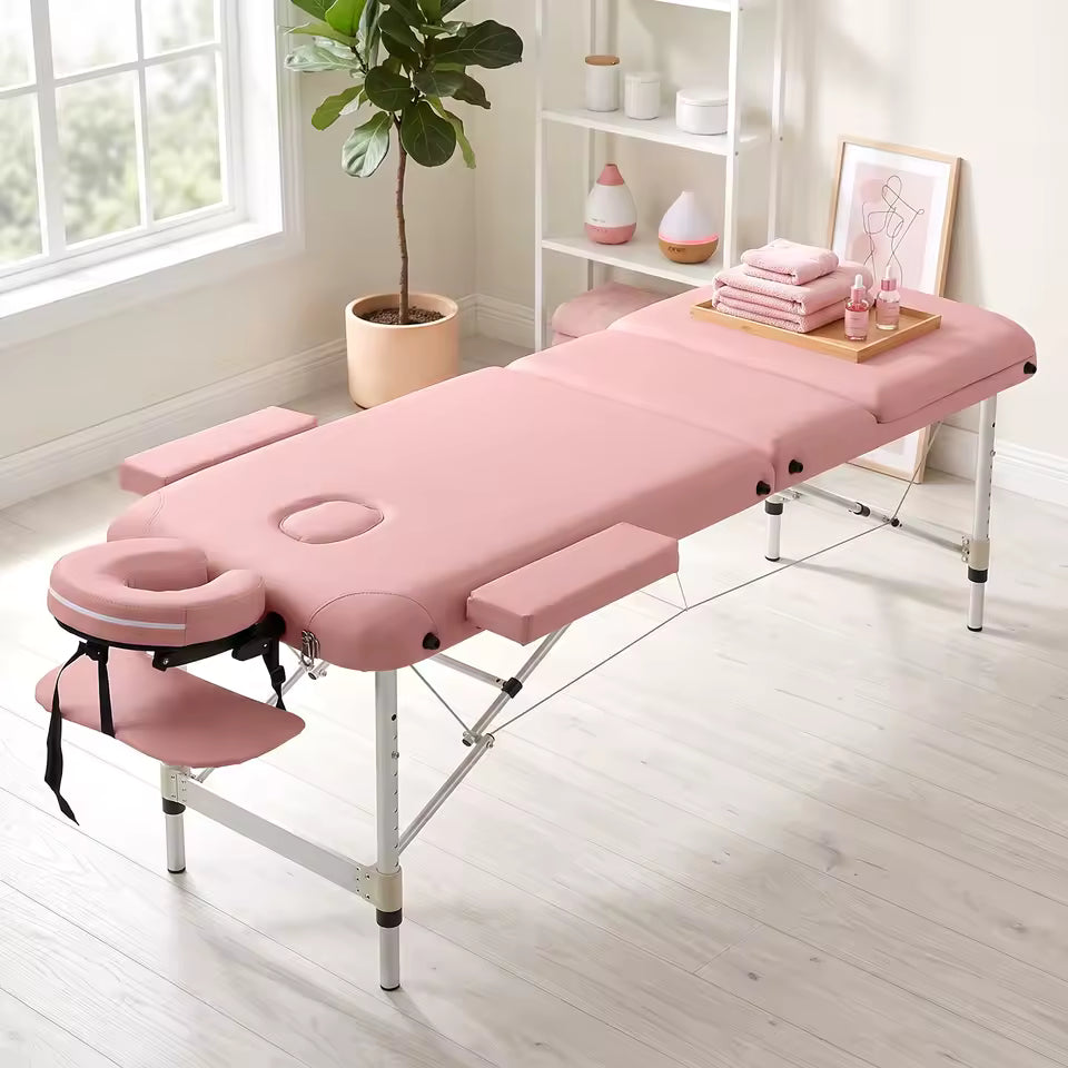 Table de massage pliante PIKKO rose installée près d'une fenêtre avec serviettes et plante verte